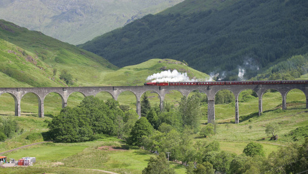 A landscape view of the Glencoe Nature Reserve with a view of a steam train on a bridge