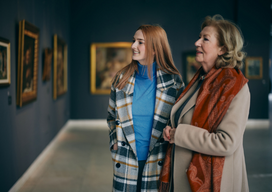 Grandmother and adolescent granddaughter are looking at the paintings in the art gallery