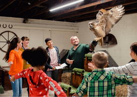 roup of school children and their teachers on a school field trip to a falconry. There is a falconer who is talking and teaching the children about the different birds of prey.