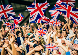 Large crowd in a football stadium cheering for their team with their hands raised and waving Great Britain flags.